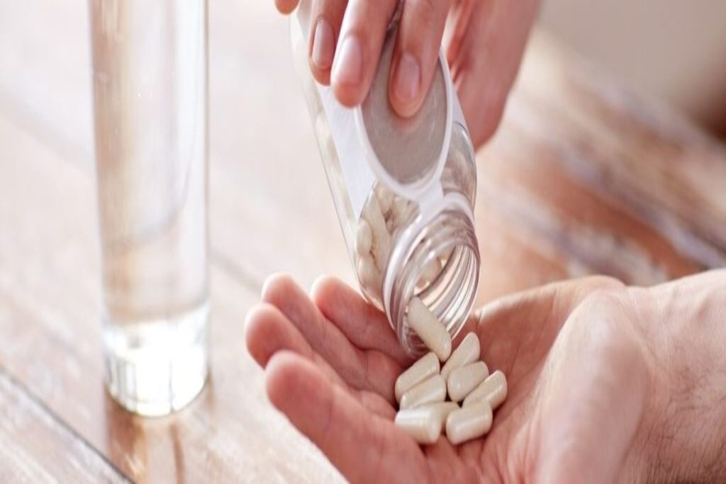 Garrafa de suplemento de glutamina ao lado de alimentos ricos em proteínas como carne, ovos e laticínios.