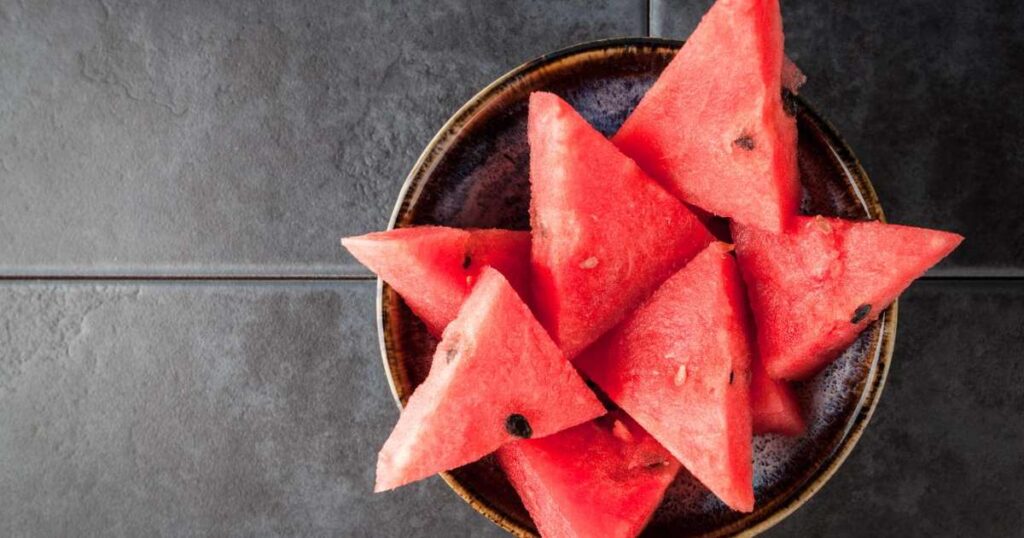Chá de melancia servindo em um copo com fatias de melancia ao fundo