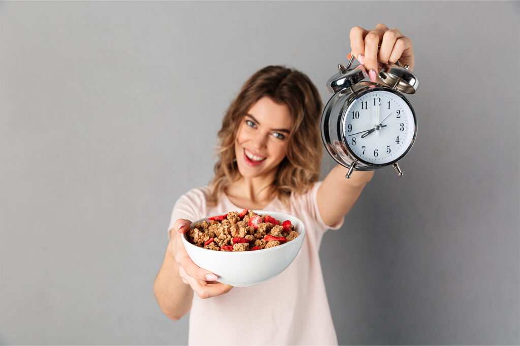 Pessoa praticando jejum intermitente com relógio e alimentos saudáveis ao fundo